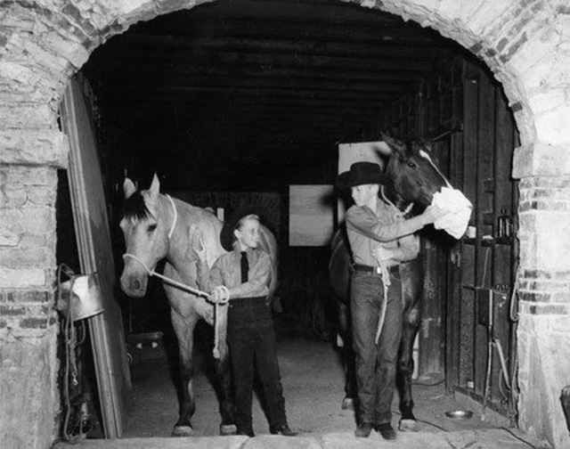 Two people with horses coming out of a stable